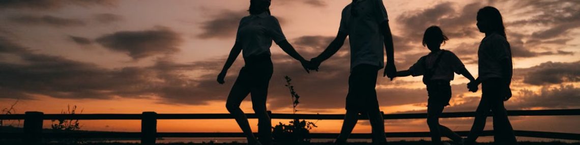 A family walks hand in hand against a vibrant sunset, evoking togetherness and peace.